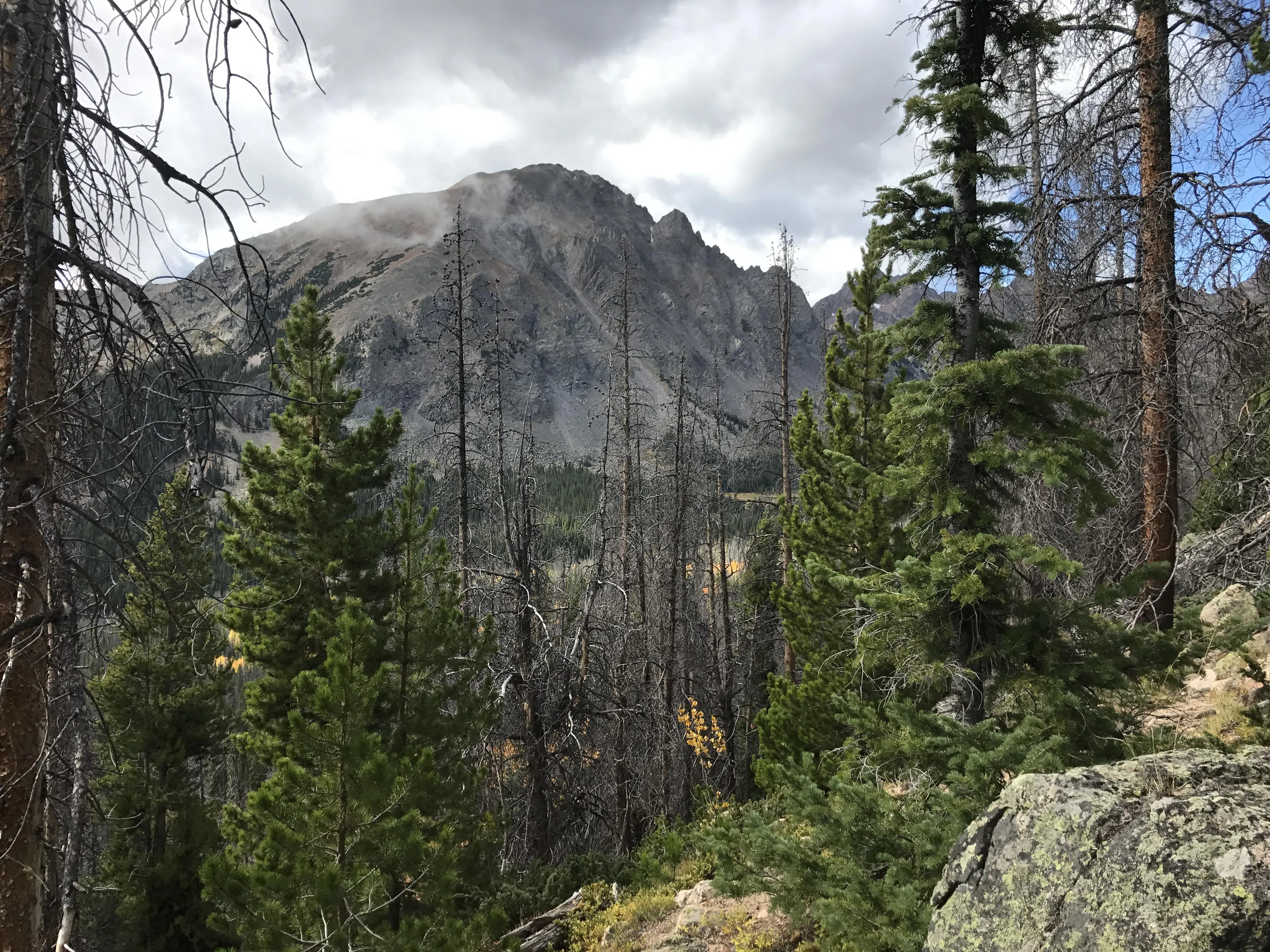 Hiker on hidden mountain trail with alpine lake and peaks in background
